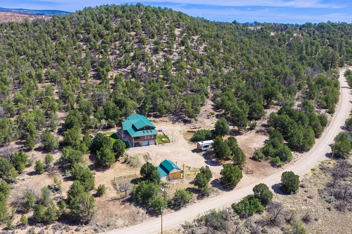Property featuring a multi-story residence with a green roof, attached garage, and a separate outbuilding, all set within a natural, treed landscape with a visible unpaved road