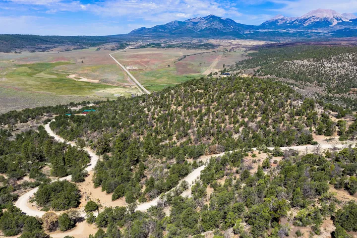 Extensive land parcel featuring natural tree coverage, unpaved access roads, and distant mountain backdrops