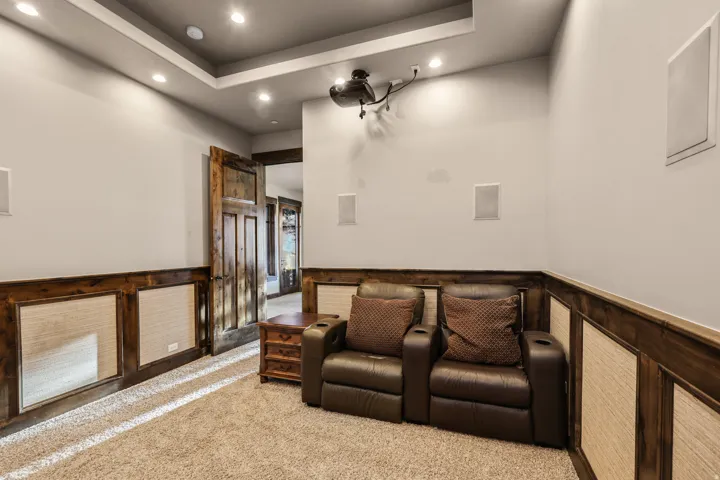 Recessed lighting, wood-paneled wainscoting, integrated wall speakers, ceiling-mounted projector, and a rustic wood door
