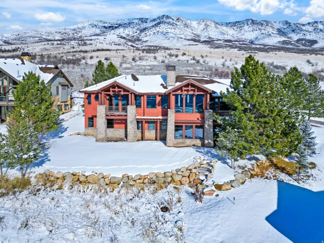 Mountain modern residence featuring an expansive red exterior, stone accents, multiple large windows, and a prominent stone chimney