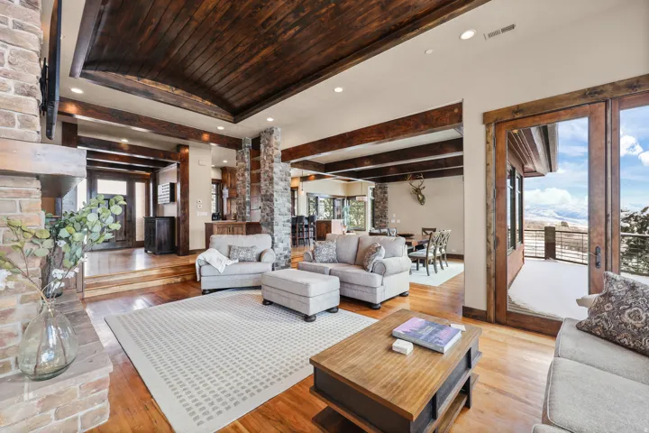 Vaulted wood-paneled ceiling, exposed wood beams, stone-clad structural elements, hardwood flooring, and a glass-paneled door leading to an outdoor balcony