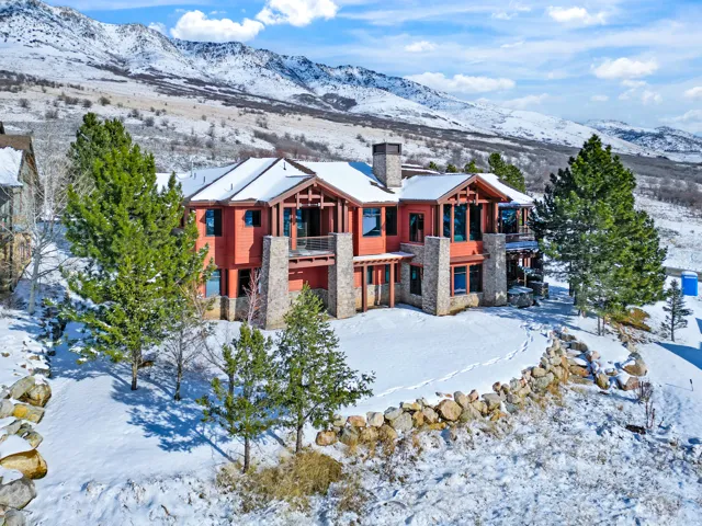 Red-clad exterior with stone accents, multiple balconies, a stone chimney, and an expansive sloped yard