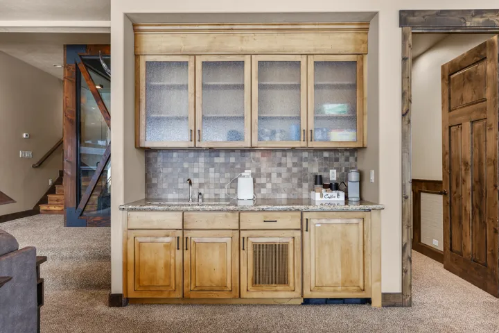 Wet bar with textured glass upper cabinetry, wood-finish lower cabinetry, and a stone-finish countertop