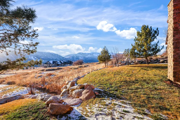 Stone-clad exterior, landscaped lawn, natural rock elements, mature trees, and mountainous terrain