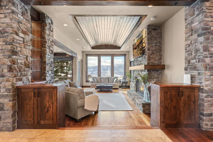 Stone-clad columns and fireplace with a wood mantle, wood-finish flooring, and a coffered ceiling with wood paneling