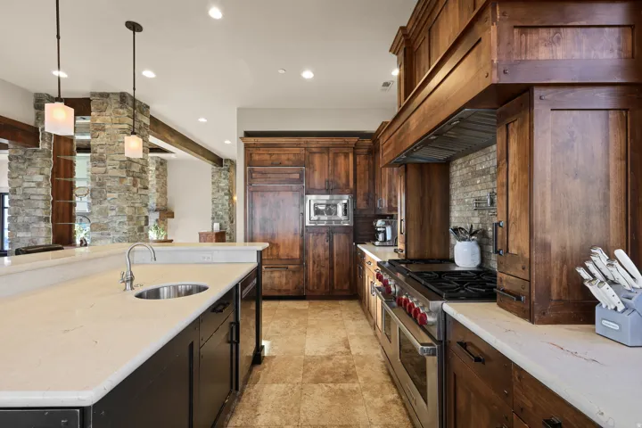 Kitchen featuring custom wood cabinetry, stone tile flooring, light-toned countertops, stone accent walls, and stainless steel appliances