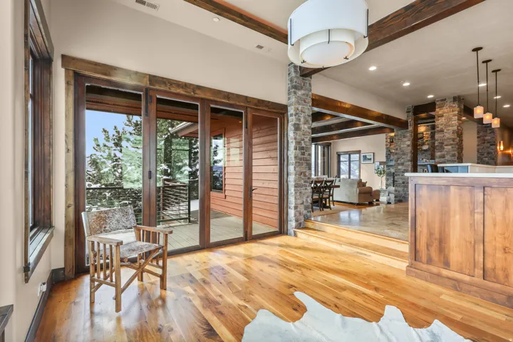 Hardwood flooring, exposed wood beams, and stone columns with a sliding glass door providing outdoor access