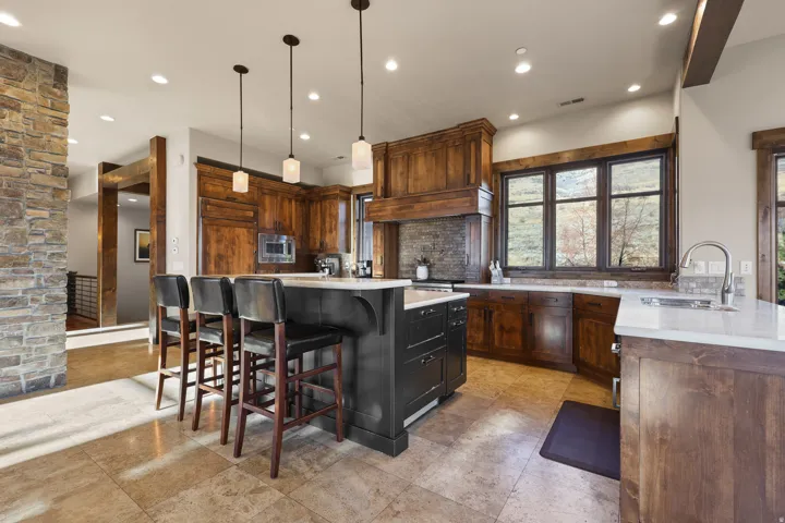 Gourmet kitchen featuring a large central island, pendant lighting, stone countertops, integrated appliances, and wood-finish cabinetry