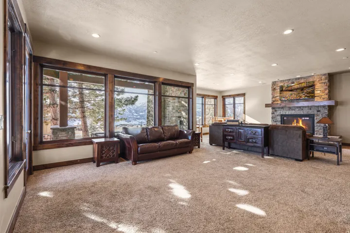 Expansive room featuring a stone-clad fireplace with a wood mantle, recessed lighting, and large windows with dark wood trim