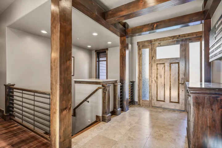 Wood-finish columns and beams, wood-finish entry door with frosted glass, recessed lighting, tile flooring, and a contemporary horizontal bar railing