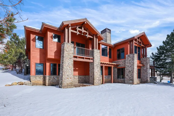 Contemporary exterior featuring cedar siding, stone accents, multiple balconies with metal railings, and a prominent stone chimney
