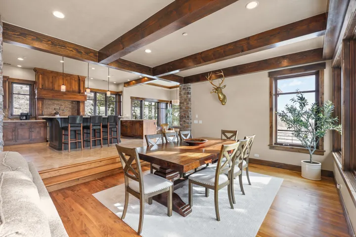 Exposed wood beams, wood-finish flooring, stone accent walls, recessed lighting, and a kitchen with a bar seating area