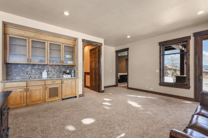 Built-in wet bar featuring wood cabinetry, frosted glass cabinet doors, a stone tile backsplash, and a sink