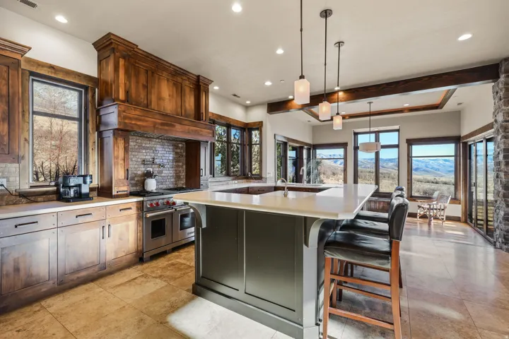 Expansive kitchen island with seating, stainless steel range with custom wood hood, stone tile flooring, and exposed ceiling beams