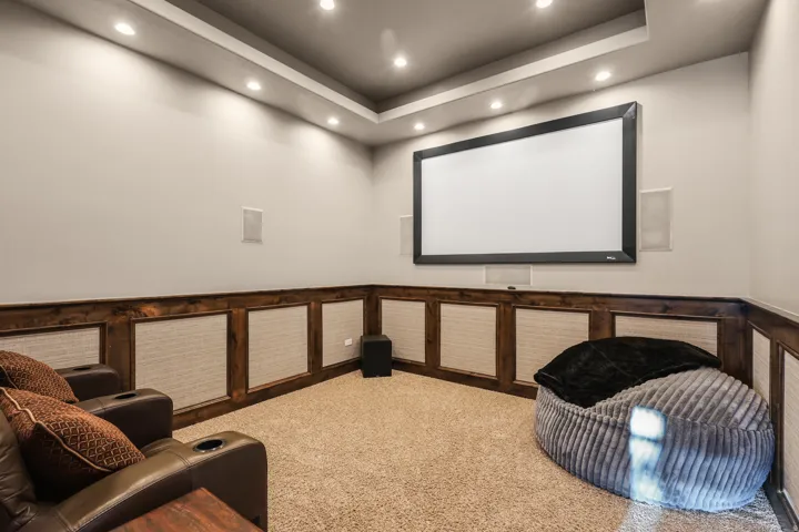 Recessed ceiling lighting, tray ceiling, built-in projection screen, integrated wall speakers, and wood-paneled wainscoting
