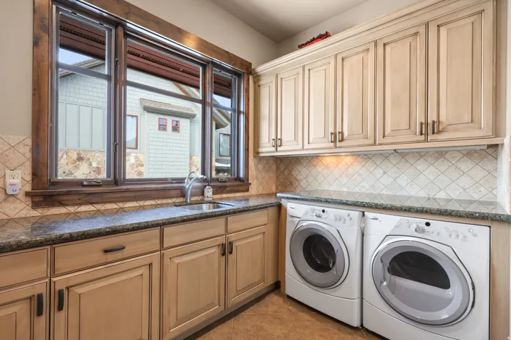 Expansive utility space featuring light wood-finish cabinetry, stone-finish countertops, a stainless steel undermount sink, and a tiled backsplash