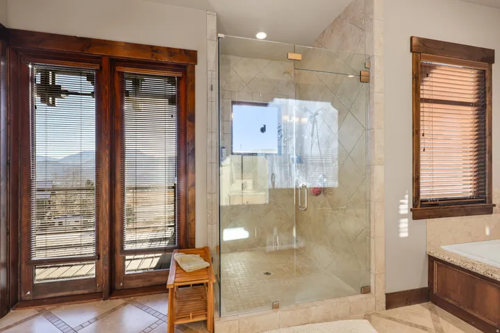 Walk-in shower with clear glass enclosure and tiled walls. Primary bath main level.