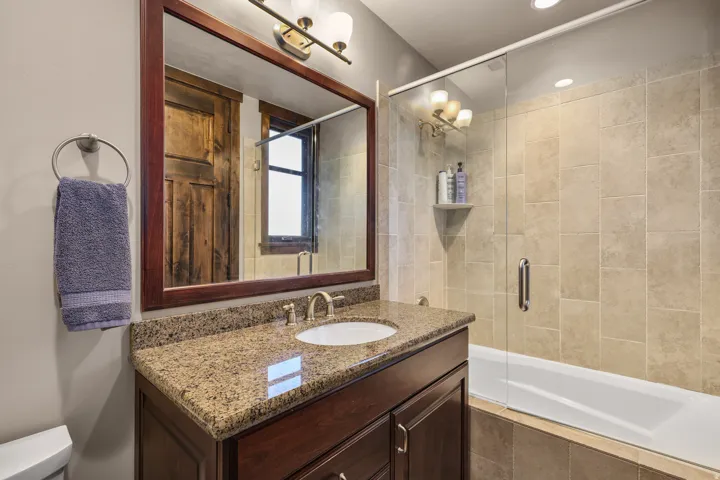 2nd bedroom with ensuite bath main level.  Spa-inspired ensuite bathroom featuring a framed mirror with wood-finish surround, granite-topped vanity with undermount sink and chrome hardware, recessed ceiling lighting, and a frameless glass-enclosed shower