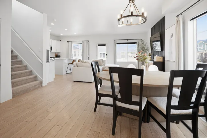 Open-concept living and dining area featuring wood-finish flooring, a black dining table with seating for four, and abundant natural light from multiple windows