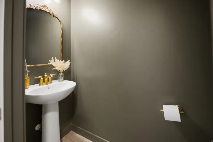 Pedestal sink with brass-finish faucet, ornate framed mirror, and warm neutral wall color