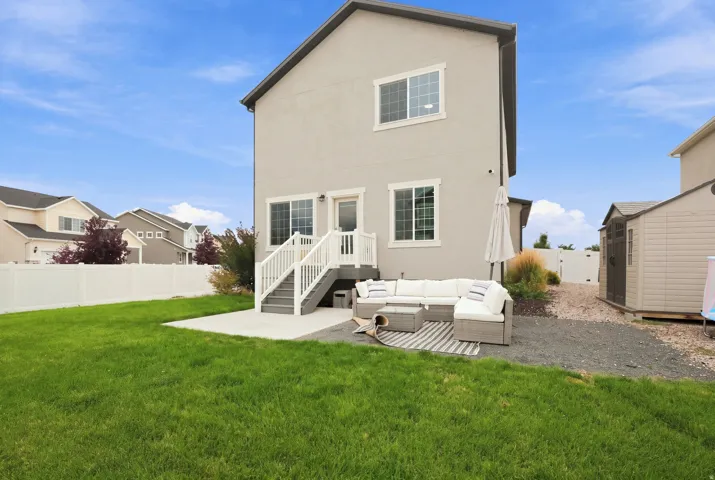 Expansive grass lawn with a concrete patio, leading to a raised deck with white railings and gray stairs