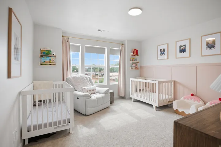 Recessed ceiling light, expansive triple windows, light-colored carpeting, two wall-mounted shelving units, and a decorative wainscoting accent wall