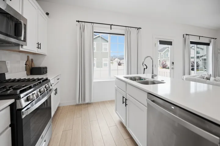 Kitchen featuring white cabinetry, stainless steel appliances, wood-finish flooring, a kitchen island with an integrated sink, and light-colored countertops