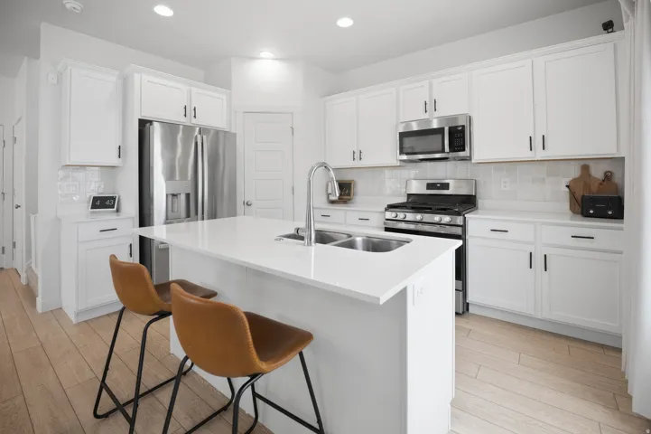 Kitchen featuring white cabinetry, stainless steel appliances, a center island with an undermount sink, white countertops, and wood-finish flooring