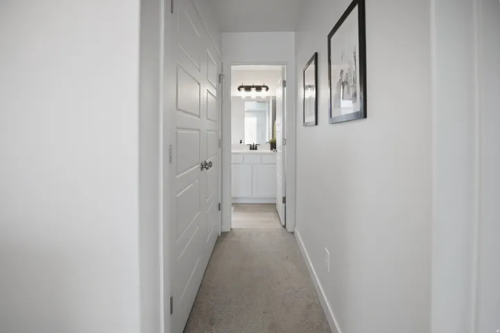 Bright hallway featuring crisp white walls, recessed lighting, and neutral carpet flooring