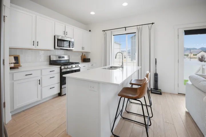 White shaker cabinetry, stainless steel appliances, central island with integrated sink, light wood-finish flooring, and a glass-paneled exterior door