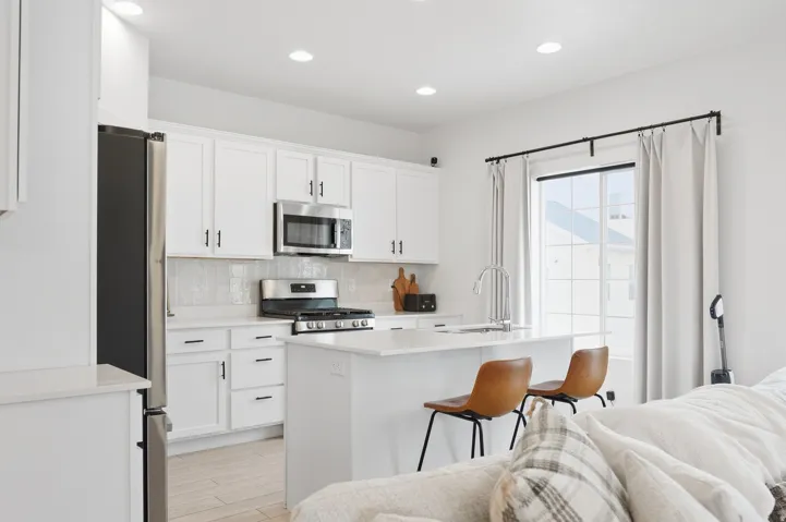 White cabinetry, stainless steel appliances, recessed lighting, kitchen island with seating, and a large window