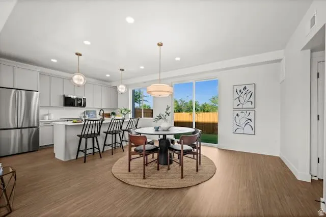 Open-concept living space with LVP flooring, a kitchen island with seating, stainless steel appliances, and sliding glass doors to the backyard