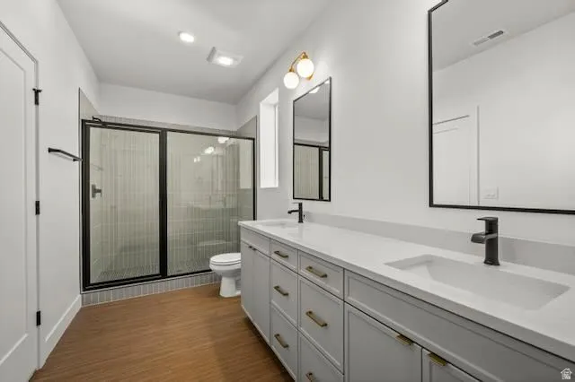 Ensuite primary bathroom. Dual vanity with integrated sinks, wood-finish flooring, and a walk-in shower with a glass enclosure