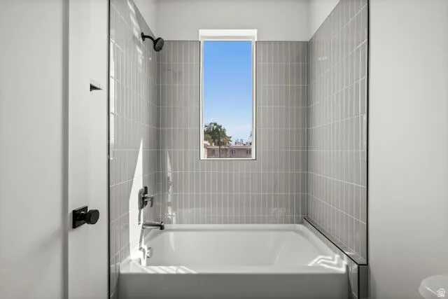 Bathtub with a single showerhead, wall-mounted faucet, and light gray vertical tile surround