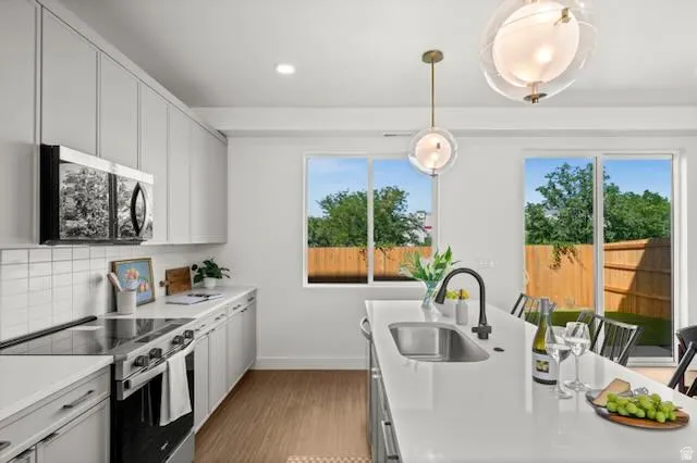 Kitchen featuring light gray cabinetry, stainless steel appliances, a white subway tile backsplash, a large center island with an undermount sink, and LVP flooring