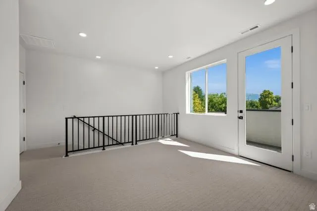 Expansive family room featuring light-colored carpeting, a black metal railing, recessed lighting, and a glass-paneled door leading to south facing balcony
