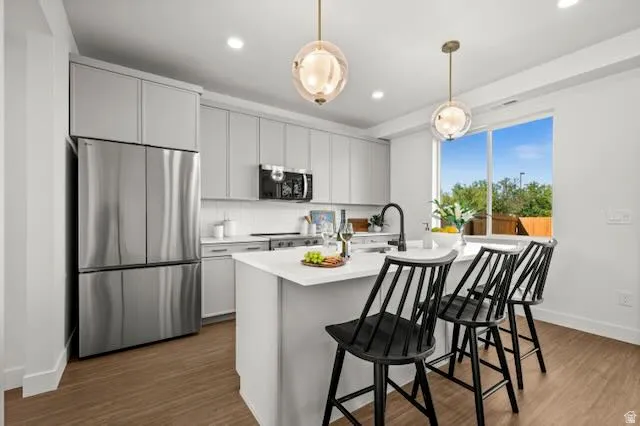 Kitchen featuring light gray cabinetry, stainless steel appliances, a center island with countertop seating, and a large window