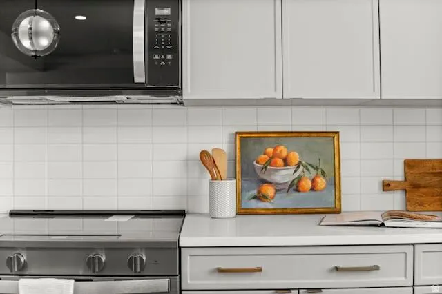 Stainless steel range with a smooth cooktop, white subway tile backsplash, light gray cabinetry with brass hardware, and white countertops