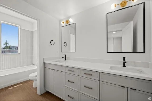 Full bathroom serving bedrooms 1 & 2. Dual vanity with light gray cabinetry, integrated sinks, white countertops, and wood-finish flooring