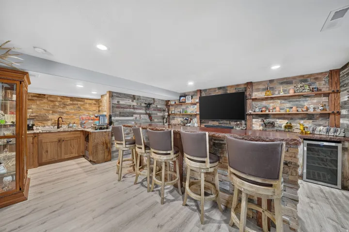 Lower-level entertaining area featuring a built-in wet bar with stone-clad facade, wood-finish cabinetry, and a wine refrigerator