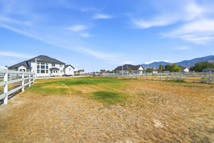 Expansive open land area with a white fence perimeter, featuring a contemporary-style residence with a dark roof and multiple large windows in the background