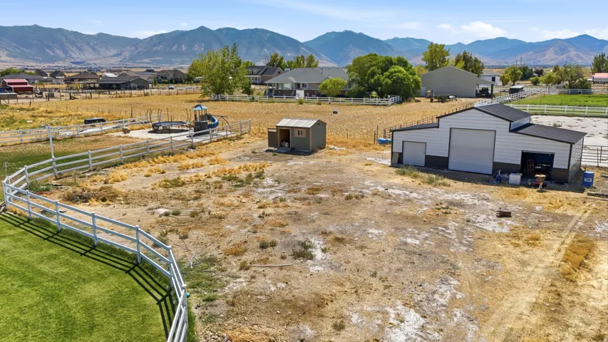 Expansive undeveloped land with a large outbuilding, a white fence, and distant mountain scenery