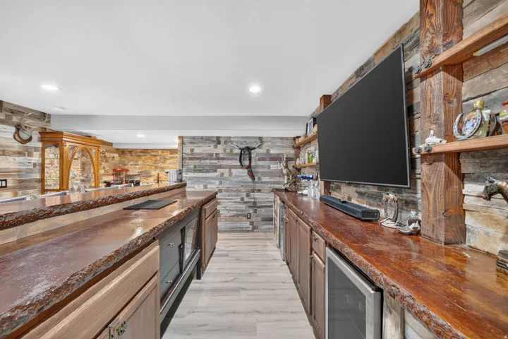 Custom wet bar with live-edge wood countertops, integrated beverage refrigerators, recessed lighting, and wood-finish flooring
