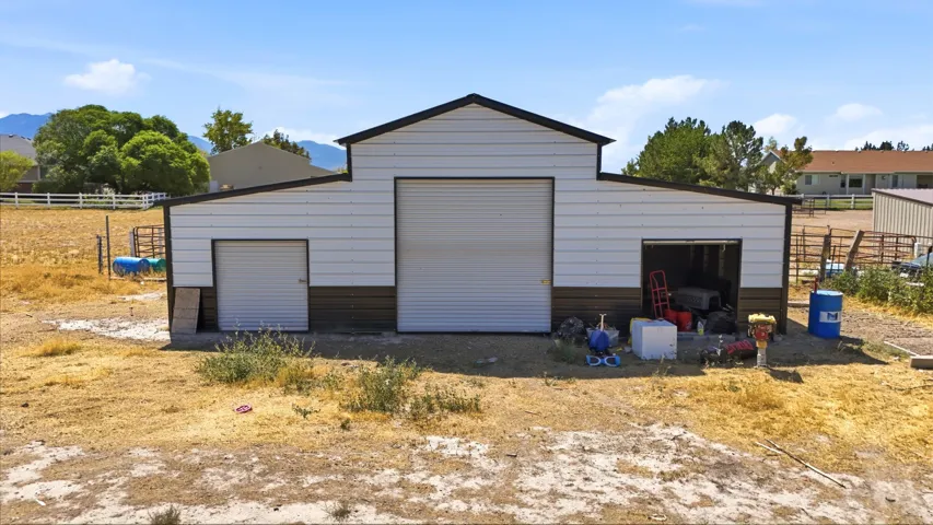 Metal barn featuring a gabled roofline, multiple roll-up doors, and a two-tone exterior finish