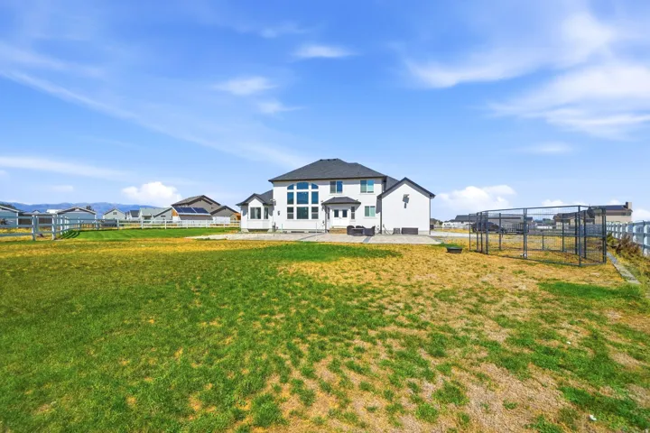 Expansive backyard with a manicured lawn, white fencing, and a large custom enclosure
