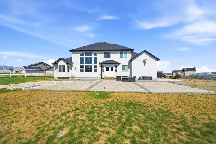 Modern stucco exterior with a dark shingle roof and a spacious paver patio