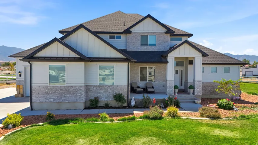 Modern exterior with light gray siding, stone veneer accents, dark shingle roof, and an inviting covered porch