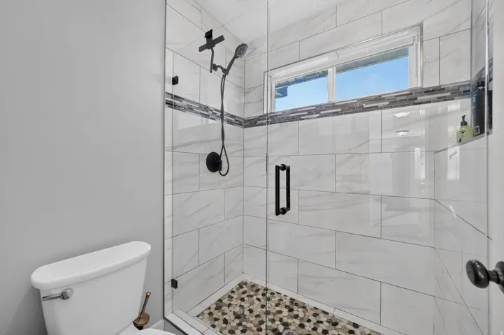 Glass-enclosed shower with a mosaic tile floor, white tiled walls, a decorative tile accent band, and matte black fixtures