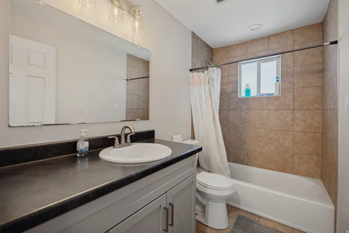 Bathroom featuring a vanity with an integrated sink, a rectangular mirror, and a bathtub with tile surround and an integrated window