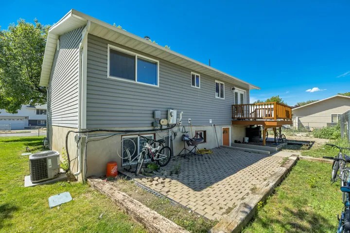 Rear exterior featuring gray horizontal siding, a raised wood deck with railing, a ground-level patio with paver stones, and a grass lawn